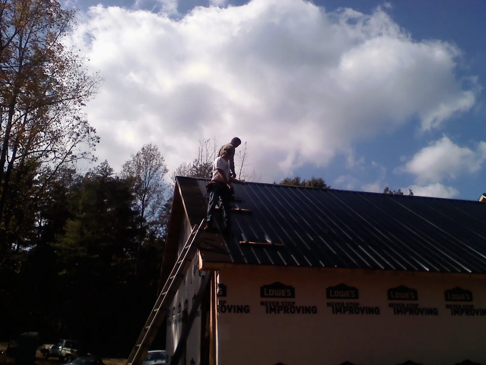 Roofer fastening dark metal panels high against a cloudy sky, from a Roof Inspection job in Centerville