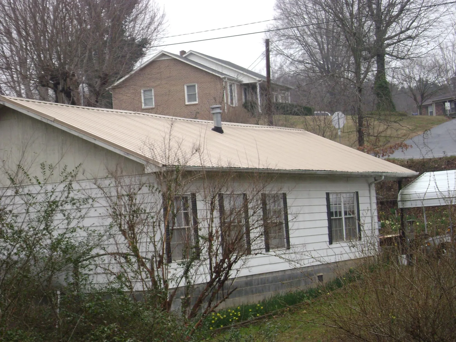 Tan metal roof on a white sided house set into a hillside — Commercial Roofing by Roofing Brothers in Centerville